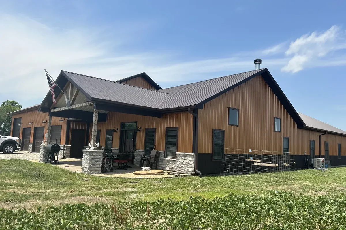 Tan and brown barndominium with a covered entry, stone columns, an American flag and an attached garage