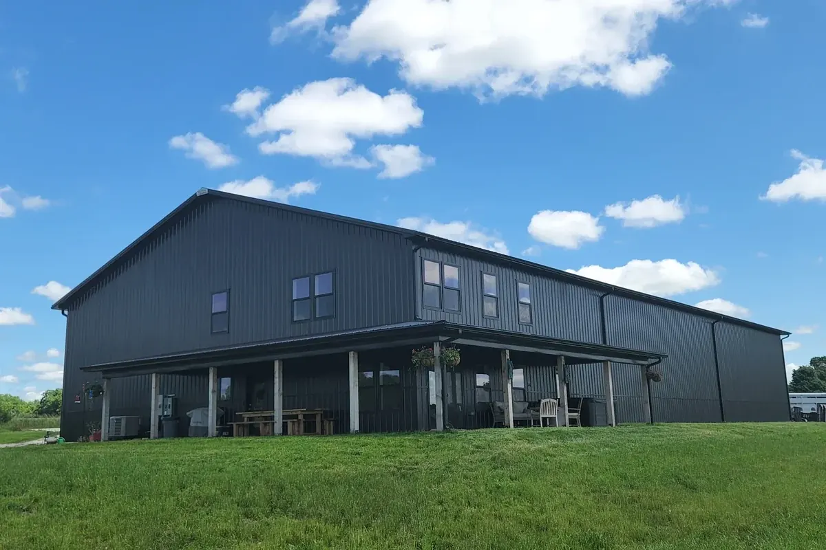 Charcoal two-story barndominium with a covered wraparound porch, hanging flower baskets and a picnic table