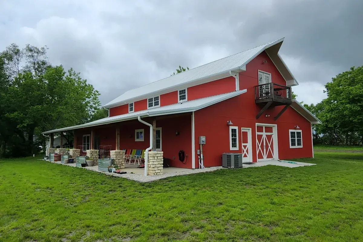 Bright red two-story barndominium with a stone-clad porch and a wood balcony off the upper level