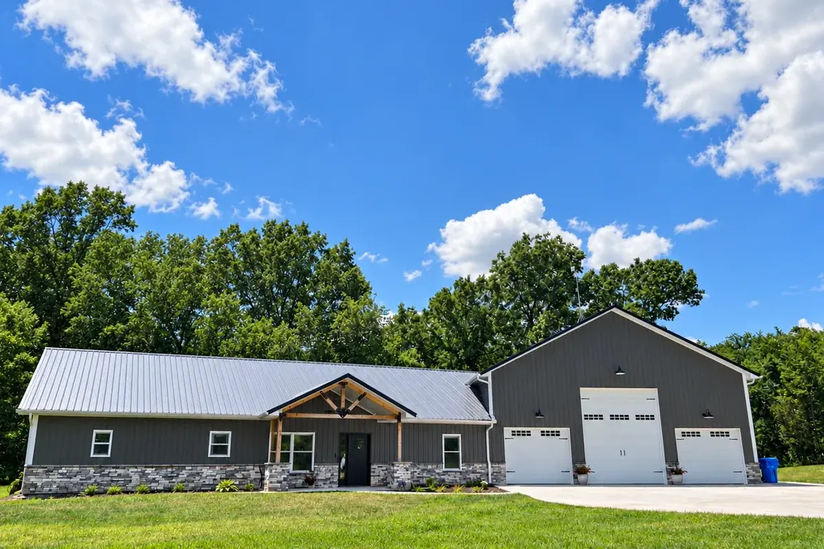 Charcoal barndominium with stone wainscoting, a timber-frame entry and an attached three-bay shop