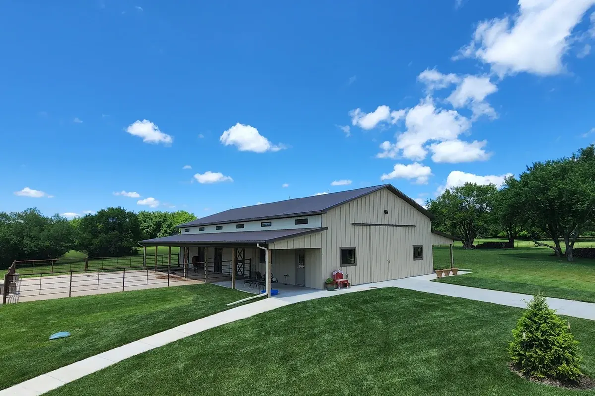 Tan equestrian barn with a covered porch and a horse near the round pen