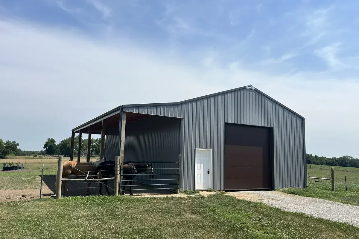 Gray equestrian barn with three horses sheltered under an open lean-to
