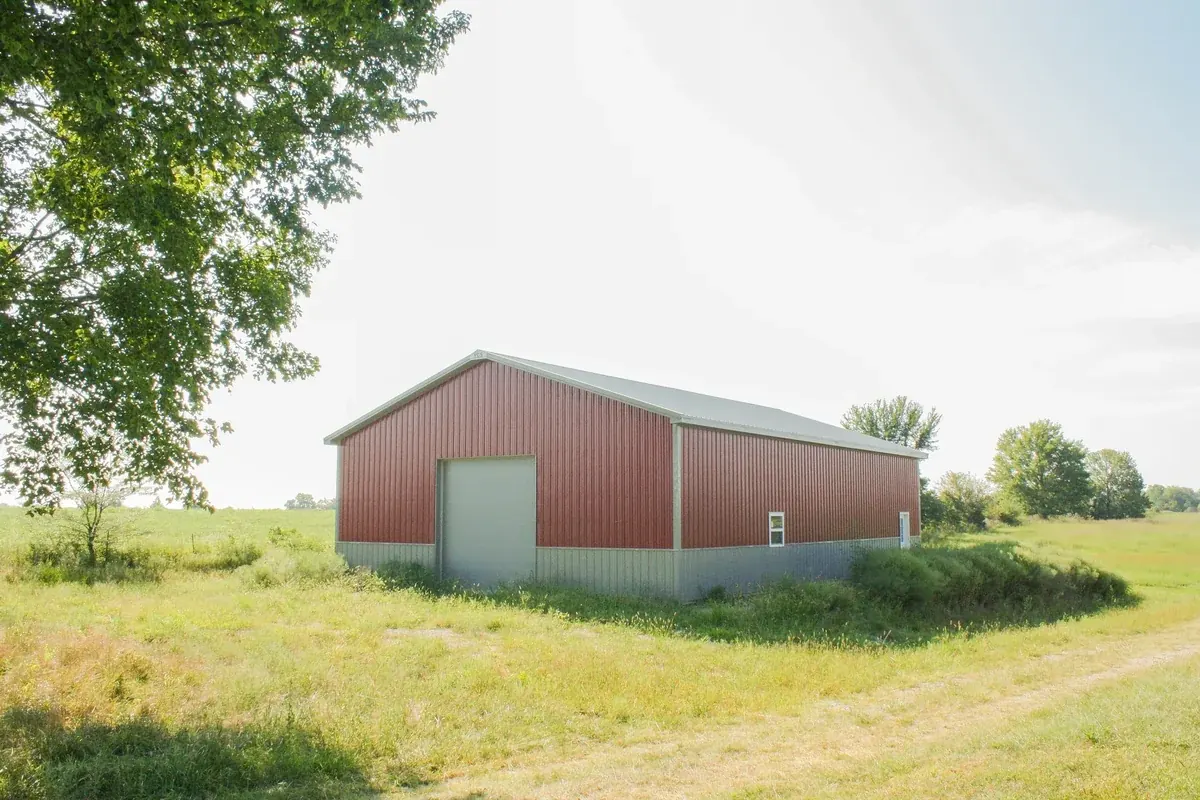 Simple red pole barn with a single overhead door in an open field