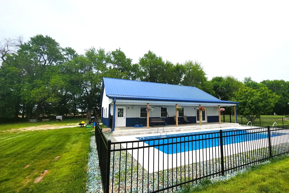 Navy and white pool house with a covered porch and hanging flower baskets beside an in-ground pool