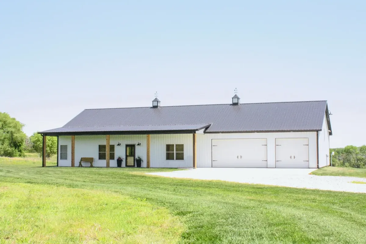 White barndominium with a covered porch and an attached two-bay shop