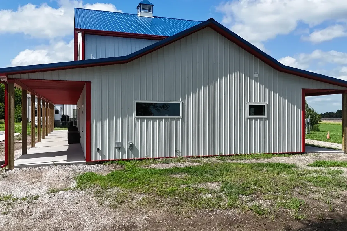 Finished white pole barn with red trim and an open drive-through bay